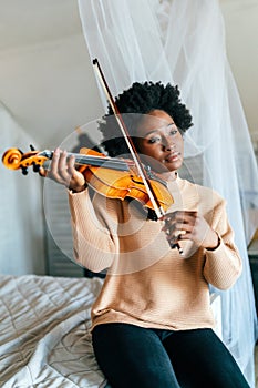 Young woman learning to play violin at home. Romantic african american girl playing violin