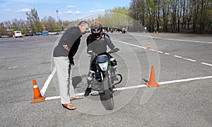 A young woman is learning to ride a motorbike in a motorcycle school. She is taught by a teacher