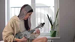 A young woman learns chords on a ukulele guitar, smiles and laughs