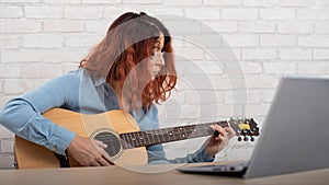 Young woman learns to play the guitar by video on a laptop. Online music lessons