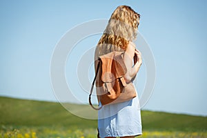 Young woman with a leather backpack in a summer field
