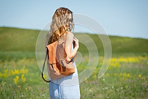 Young woman with a leather backpack in a summer field