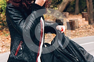 Young woman in leather jacket puts things in backpack on the background of a bike path in the autumn forest