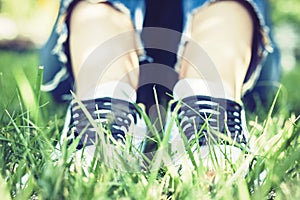 Young woman legs in pair of sport shoes sneakers  of blue suede on the grass lawn in park