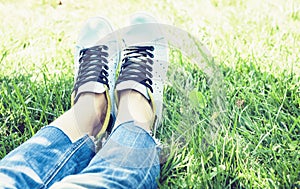 Young woman legs in pair of sport shoes sneakers  of blue suede on the grass lawn in park