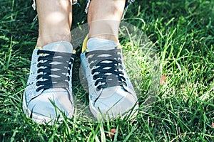 Young woman legs in sport shoes sneakers of blue suede, sitting on the grass lawn in park