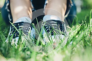 Young woman legs in sport shoes sneakers of blue suede, sitting on the grass lawn in park