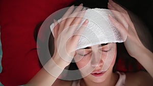 A young woman lies in bed with a poultice on her forehead, experiencing severe pain in her head. Close-up portrait. The view from