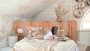 a young woman lies in bed and uses a laptop for video conferences or chatting with friends