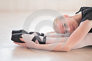 A young woman lies bent over on her feet in a ballet class. Ballerina stretches on the floor.