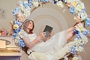 A young woman lies with a book in flowers. Studio portrait of happy woman reading book in white dress
