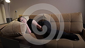 Young woman lies on brown sofa with large pillows and sleeps