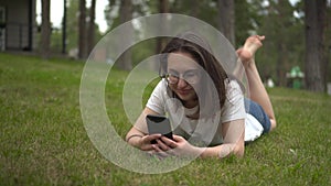 Mladá žena spočívá na tráva chatování na. brýle je odpočívá v telefon 