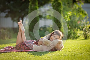 A young woman lies on the grass of a spring lawn with a teddy bear. Concept: Expecting a Child, Goodbye Childhood