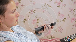 Young woman lies at home on the couch with coats from the TV. Looks attentively at the screen