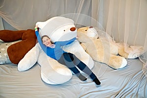 A young woman lies on a large toy soft white bear