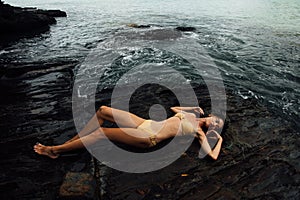 young woman lies on a rock ocean shore. Beautiful girl on stony background