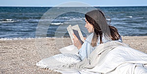 A young woman lies by the sea on the beach and reads a book