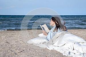 A young woman lies by the sea on the beach and reads a book