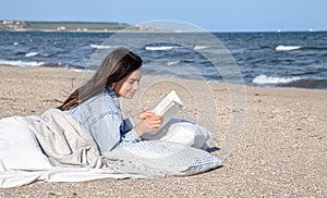A young woman lies by the sea on the beach and reads a book