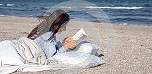 A young woman lies by the sea on the beach and reads a book