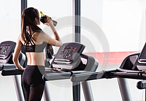 Young woman lifestyle standing drinking water on treadmill workout exercise cardio