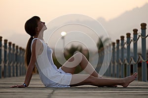 Young woman in light dress enjoying warm sunny evening on sea shore. Summer vacations and travelling concept