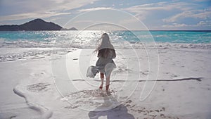 A young woman in a light dress runs barefoot through the waves towards the sea. A long-awaited meeting with the sea.