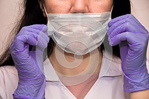 A young woman in lilac medical gloves puts a protective mask on her face . A confident girl, a female doctor in a