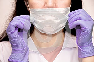 A young woman in lilac medical gloves puts a protective mask on her face . A confident girl, a female doctor in a