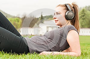Young woman listening music on headphones while lying on grass