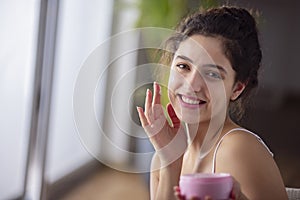 Portrait of a young woman applying moisturizer cream on her face