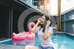 Young woman listening music by using headphone near swimming pool of resort or hotel background with happiness and smile face