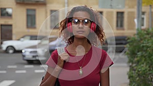 Young woman listening to audio podcast and walking along street on summer day spbas.