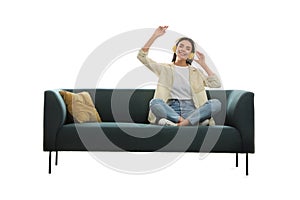 Young woman listening to music on comfortable green sofa against white background