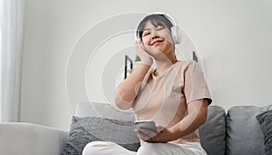 Young woman listening to music with headphone and relaxing while sitting on the sofa at home