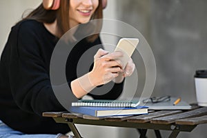 Young woman listening to music on headphone, typing text message, chatting online on mobile phone