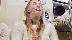 Young woman listening to music in the subway car. Media. Girl wearing white sweater with pink headphones sitting in