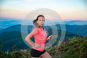 Young woman listening to the music during trail running in mountains