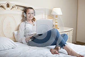 Giovane donna ascoltando sul musica un computer portatile sul un letto 