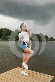 Young woman listens to music and enjoys vacation, weather before thunderstorm, lake, summer.