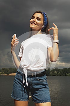 Young woman listens to music and enjoys vacation, weather before thunderstorm, lake, summer.