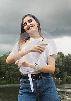 Young woman listens to music and enjoys vacation, weather before thunderstorm, lake, summer.