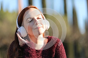 Young woman listens to music with white wireless headphones while sunbathing