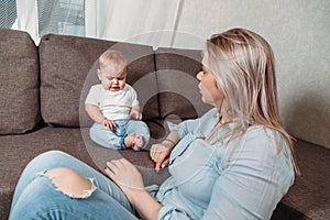 Young woman and little baby boy at home on bed. Mom teaches a small child to perceive criticism