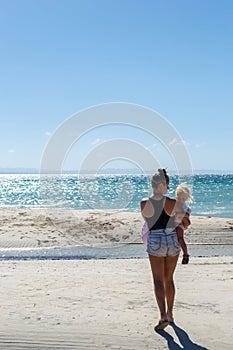 Young woman with little blonde baby walking by the sea in Philippines