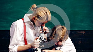 Young woman with a little boy looking at a wheat stem in a microscope on a green board background. Teacher and student