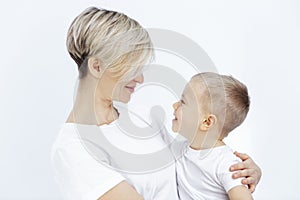 A young woman and a little boy smile and hug. Mom and son in white T-shirts on a white background. Love and tenderness