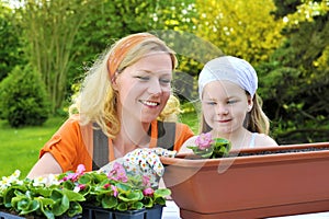 Young woman and little girl gardening in spring, planting flower seedlings, smiling mother and her happy child working in garden