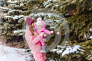 A young woman and a little girl hang balls on a eding tree in winter